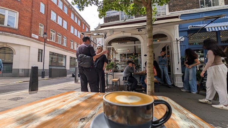 A latte in a dark cup on a table outside the shop
